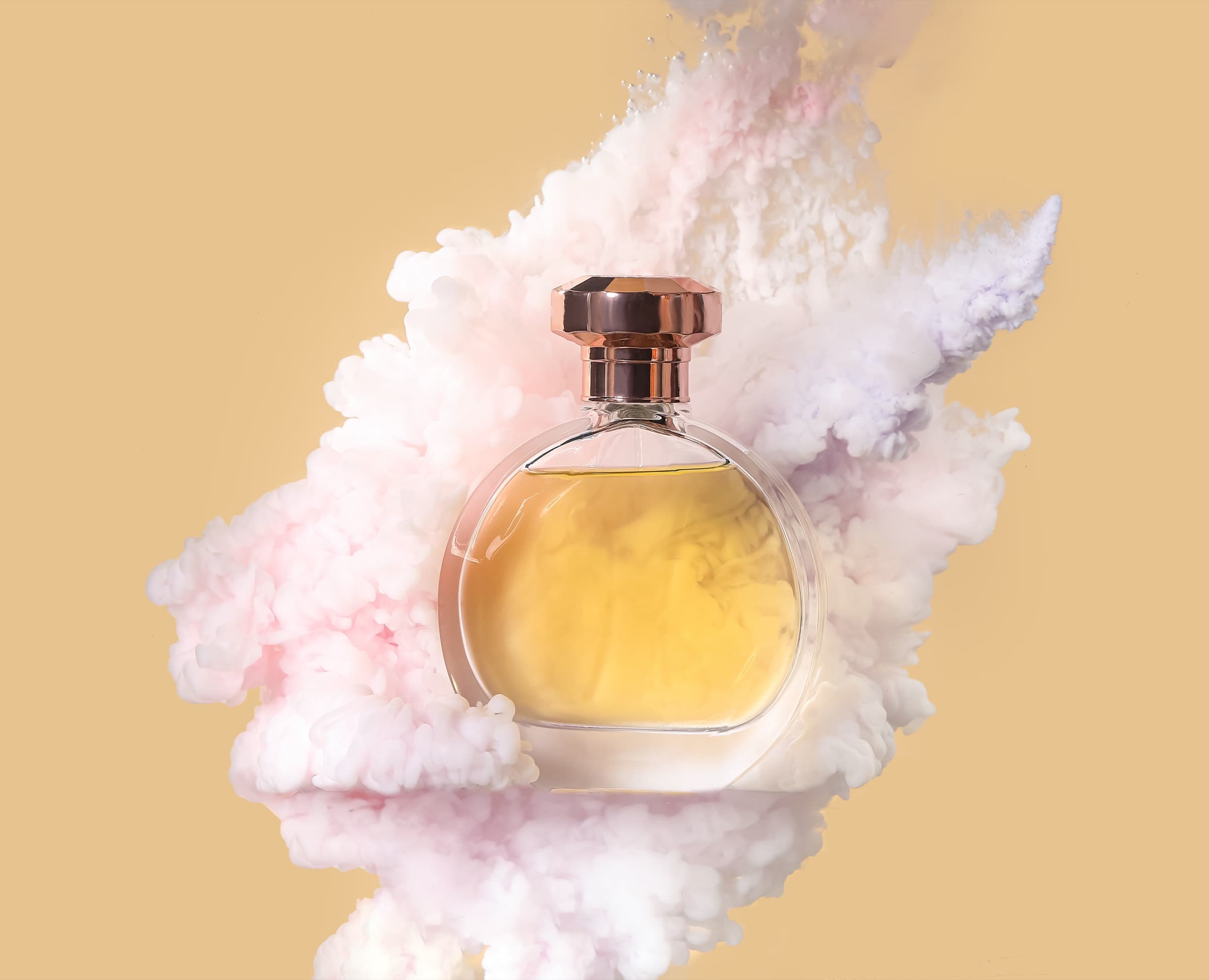 A round perfume bottle with amber liquid and a copper cap in a cloud of pale pink smoke on a beige background